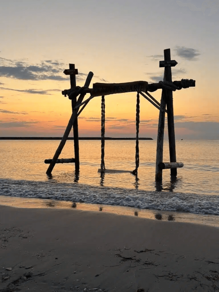 Leagănul din lemn cu semnul Plaja Pescărie în apa mării, la apus