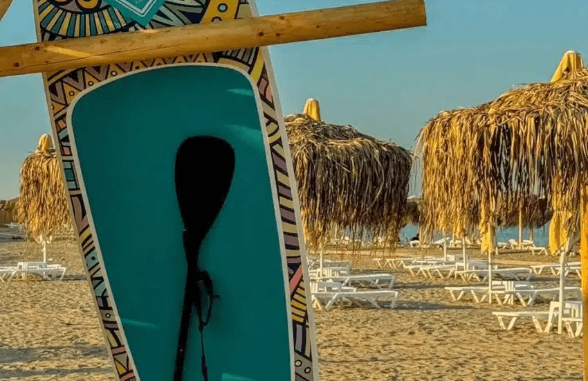 Placă de SUP colorată lângă umbrele de paie și șezlonguri pe nisip la Plaja Pescărie